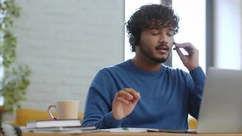 Einbindung eines Mannes in ein virtuelles Meeting mit Laptop und Headset an einem lichtdurchfluteten Arbeitsplatz