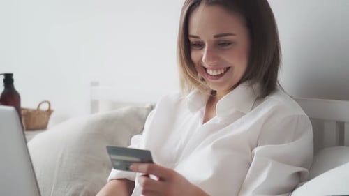 Happy Woman Buys Online and Smiles Girl Enters Credit Card Number on Laptop Shopaholic Buys on the