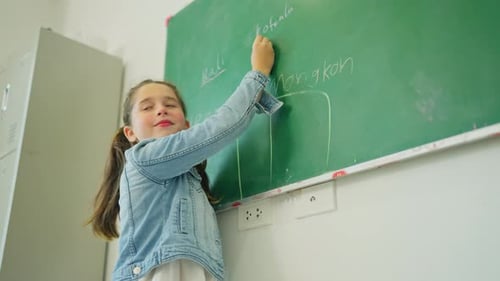 Young girl enjoy to write her name on greenboard also spelling in front of classroom of home school.