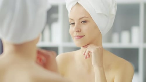 Junges Mädchen sitzt vor einem Schminkspiegel im Badezimmer und trägt eine Hautcreme auf