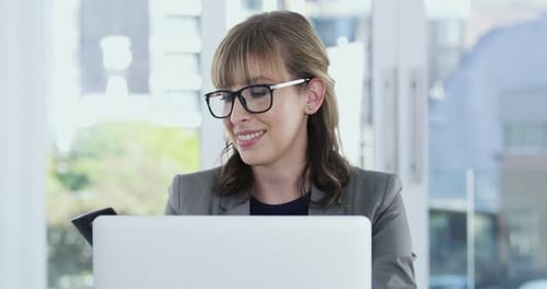 4k video of a young businesswoman answering a phone call while working on a laptop in an office