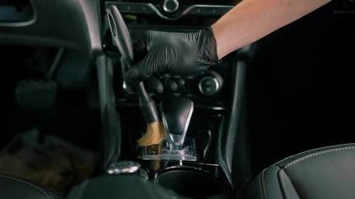 Car wash worker thoroughly cleaning the interior of a luxury car with a brush, gear box, detailing