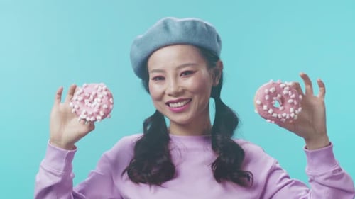 Playful Woman Holding Pink Donuts in front of Eyes