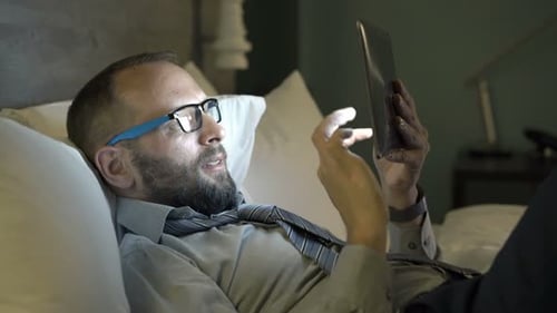 Young Businessman Working with Tablet Lying on Bed in Hotel Room At