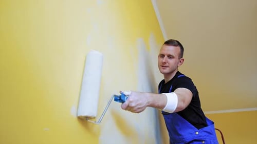 Attraktiver Maler, der das Innere der Wand neu gestaltet. Fröhlicher Mann, der mit Gemälden arbeitet.