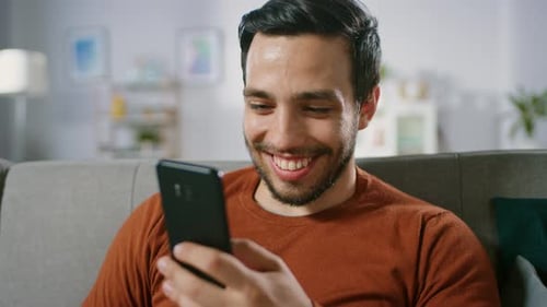 Man Smiling Using Mobile Phone on Couch at Home