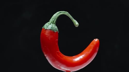 A small sharp red pepper rotates on a black background and smoke comes from it. Close-up.