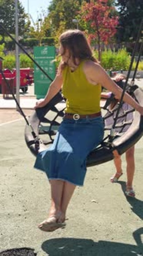 Happy Mother Swinging with Her Daughter in a Sunny Playground