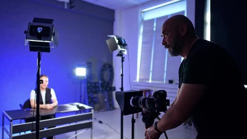 Bearded cameraman prepares camera for footage in studio.
