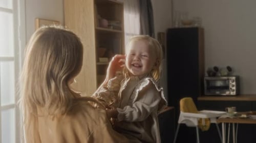 Verspieltes kleines Mädchen in den Armen der Mutter