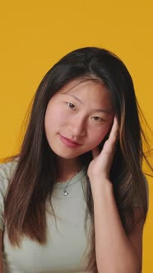 Young woman looking at camera, smiling and flirting isolated on yellow background in studio