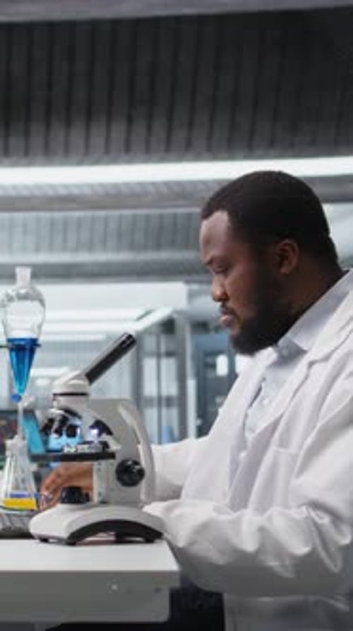Adult Man Scientist Using Microscope in Laboratory
