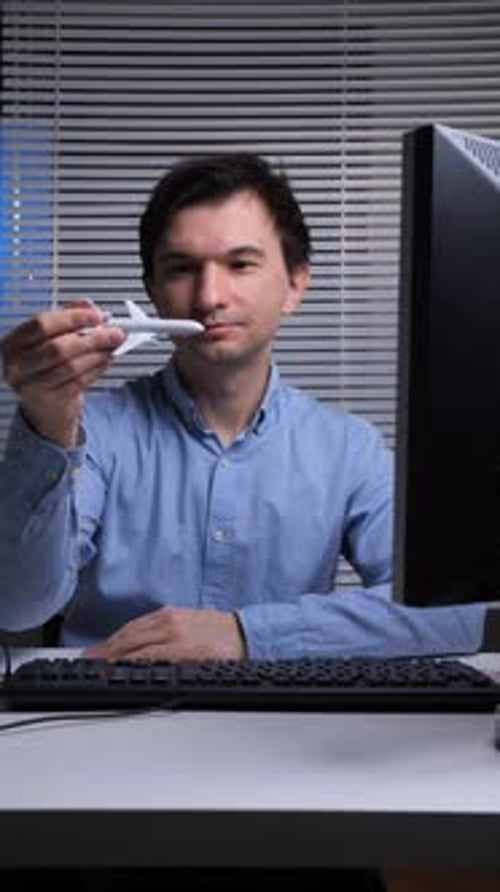 Vertical Video Young Man Holding a Small White Toy Airplane While Sitting at His Desk in an Office