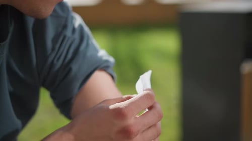 Young Man Seated Applying Nicotine Patch on Upper Arm with Green Blurred Background