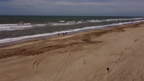 Aerial shot of four people riding horses along sandy beach with waves of Atlantic Ocean during summe