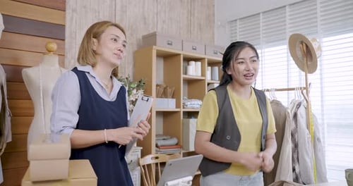 Asiatische Bekleidungsdesignerin diskutiert Idee mit einer erwachsenen Kollegin, die neben dem Kleiderständer steht