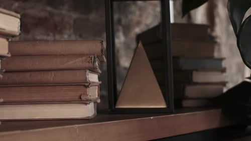 Old Vintage Books in Craft Paper Cover Lie on Shelf Near Pyramid Figure