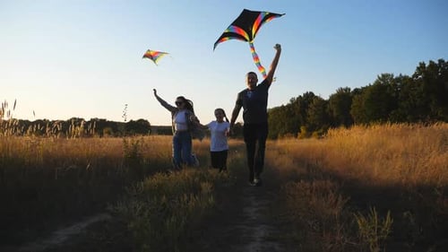 Mom and Dad with Little Daughter Jogging with Rainbow Kites on Rural Trail at Sunset