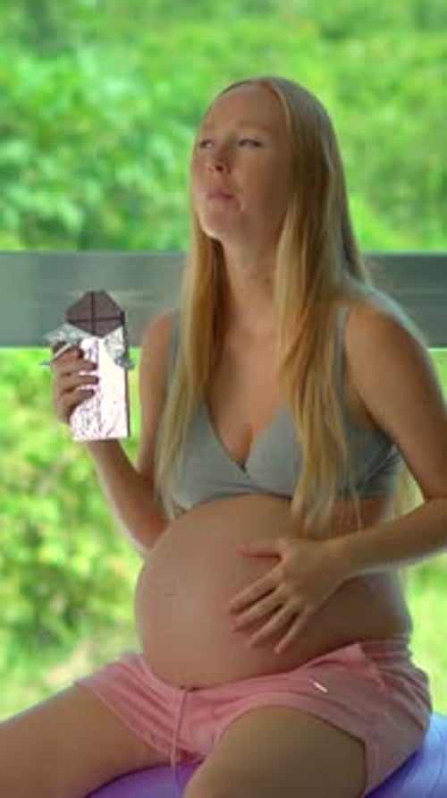 In This Slowmotion Stock Video a Pregnant Woman Indulges in a Chocolate Bar Exploring the Concept of