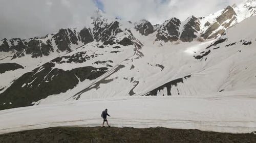 Aerial View of a Man Hiking with Backpack in High Snowy Mountains Climber Traverses Snowcovered