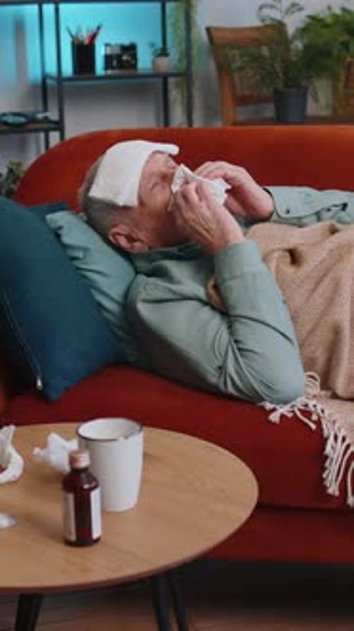 Un homme âgé malade souffrant d'une allergie au froid, allongé sur le canapé de la maison, éternue avec de la morve dans une serviette