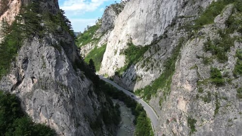 The Drone Accompanies a Car Driving Along the Highway Flying Through a Picturesque Rocky Canyon It