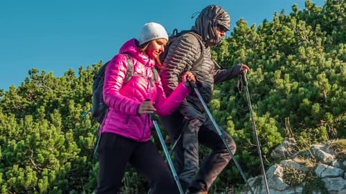 Hiker couple trekking through the rocky and uneven mountainous terrain on a bright sunny morning. Sl