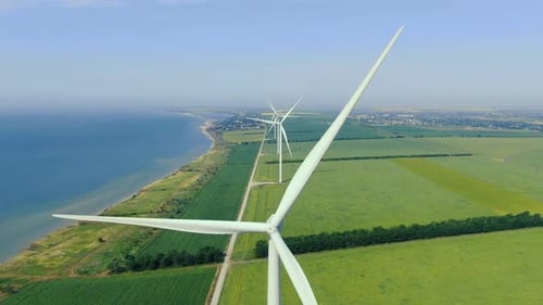 Aerial shot of the wind turbines on the shore of the sea with the view on a city