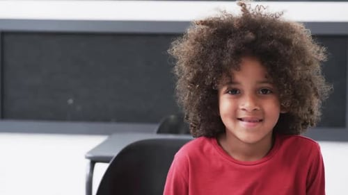 In a school classroom, a young African American boy smiles warmly with copy space
