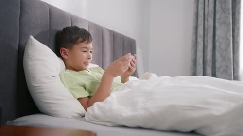 Boy Lies in Bed Using Mobile Phone