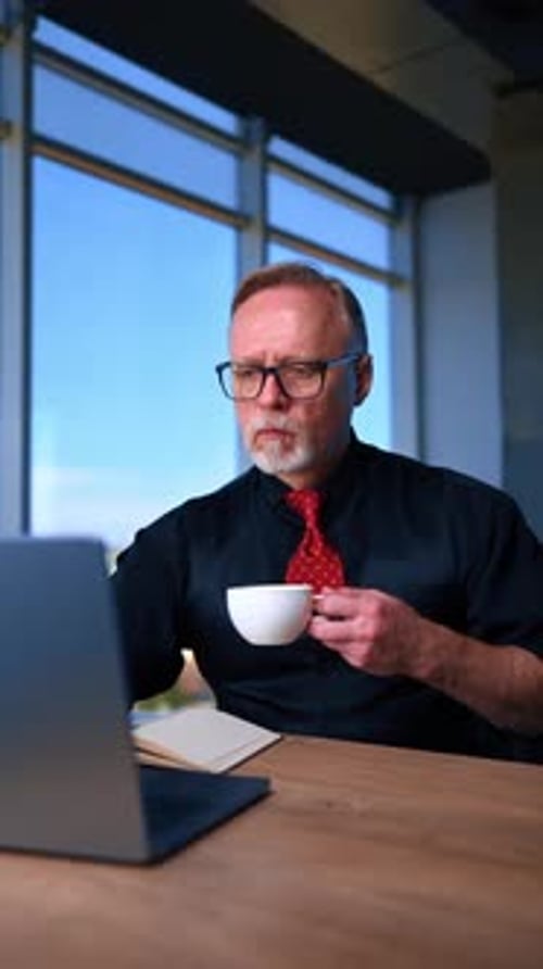 Man Drinks Coffee While Working on Laptop