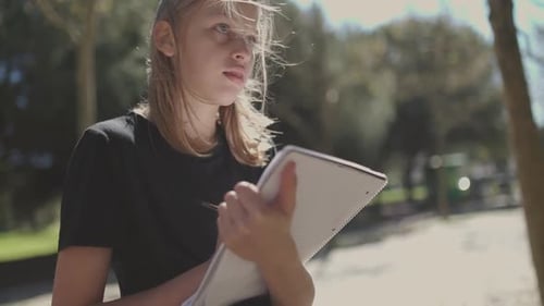 Girl Writing in Notebook Outdoors on Sunny Day