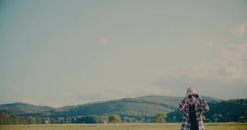 Male Tourist Looking Through Binocular Standing In Meadow
