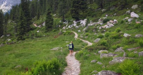 Aerial shot of a carefree woman is trekking on the path in the middle of mountains surrounded by n