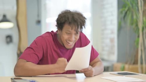 African Man Celebrating Success while Reading Documents in Office