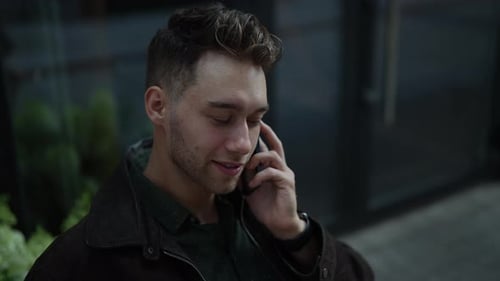 Fröhlicher bärtiger Mann genießt ein angenehmes Telefongespräch, während er lächelt und eine Pause in der Stadt einlegt