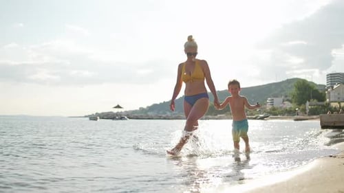 A Mother and Son Walk Holding Hands on the Seashore Splashing Water