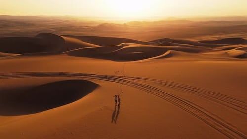 Aerial View of Two Individuals Walking on Sand Dunes in Peru During Sunset