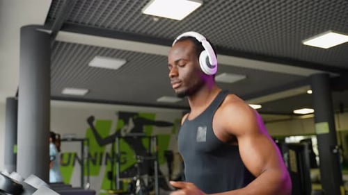 A Man with Headphones Running in a Modern Gym on a Treadmill
