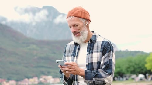 Older Elder Hipster Man Standing in Nature Park Wearing Earbud Using Phone