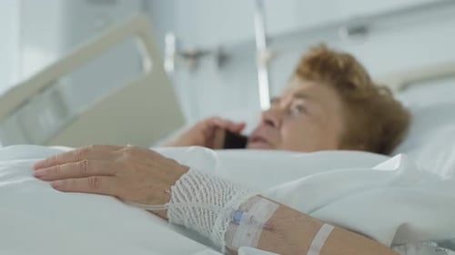 Elderly Patient Resting in Bed on phone call Moving fingers, focus foreground - Hospital Concept