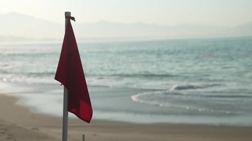 Red Beach Safety Flag Waving on Sandy Shore