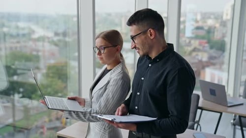 Office colleagues talk looking at the screen of laptop in lady’s hands.