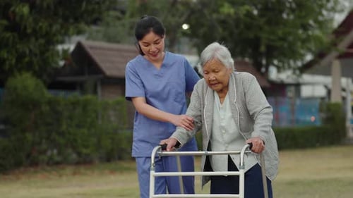 caregiver nurse support senior woman walking with walker in the park