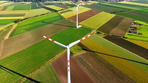 Windmill blades rotate in the field. Aerial view on the wind turbine in the agricultural countryside