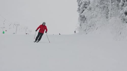 Skier in Red Jacket and Helmet Riding Down Groomed Snowy Slope at Mountain Ski Resort During Cloudy