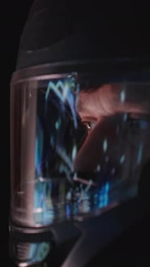 Vertical video. Focused Man in Helmet Lifting Visor with Hand in Dim Lighting, Close-Up Side Angle,