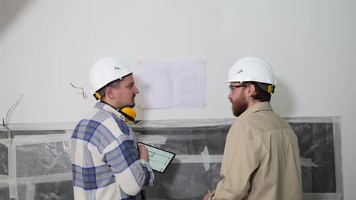 Des ingénieurs discutent d'un plan accroché au mur et le comparent à un document sur une tablette