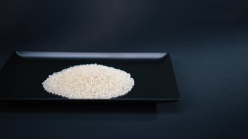 Nahaufnahme weißer runder Reis liegt auf schwarzem und blauem Hintergrund auf einem schwarzen langen flachen Teller Japanisch