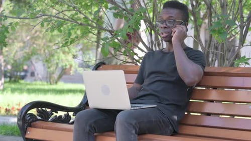 Young Adult Using Laptop and Phone on Park Bench